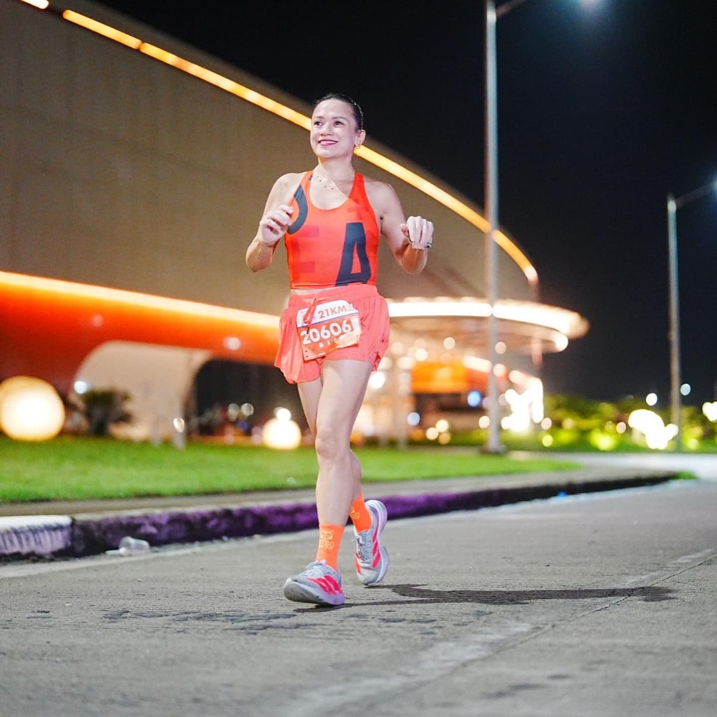 Runner in an orange race kit smiling mid-stride on a lit city course at night