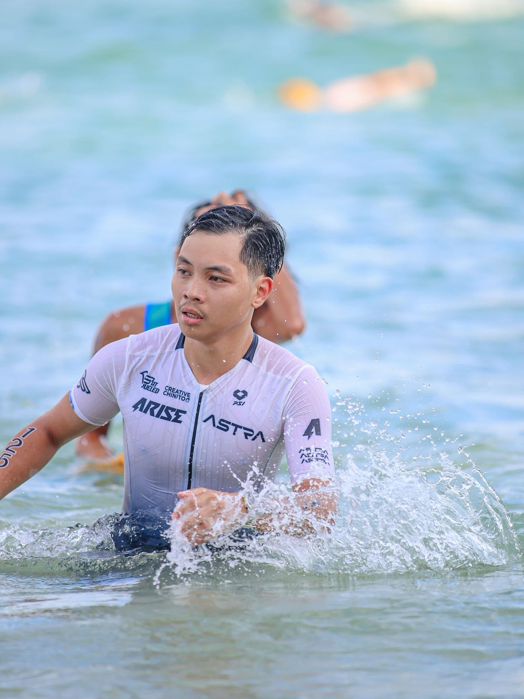Triathlete in a white trisuit wading out of the sea through splashing water