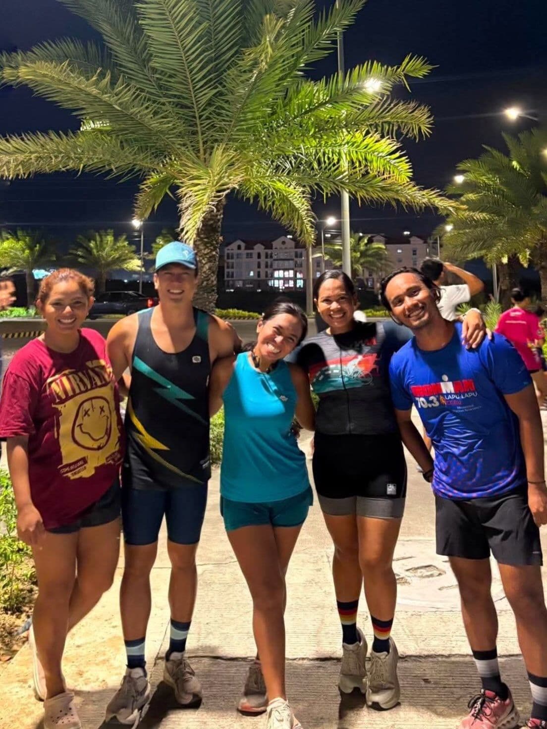 Five friends in running gear posing together under palm trees at night
