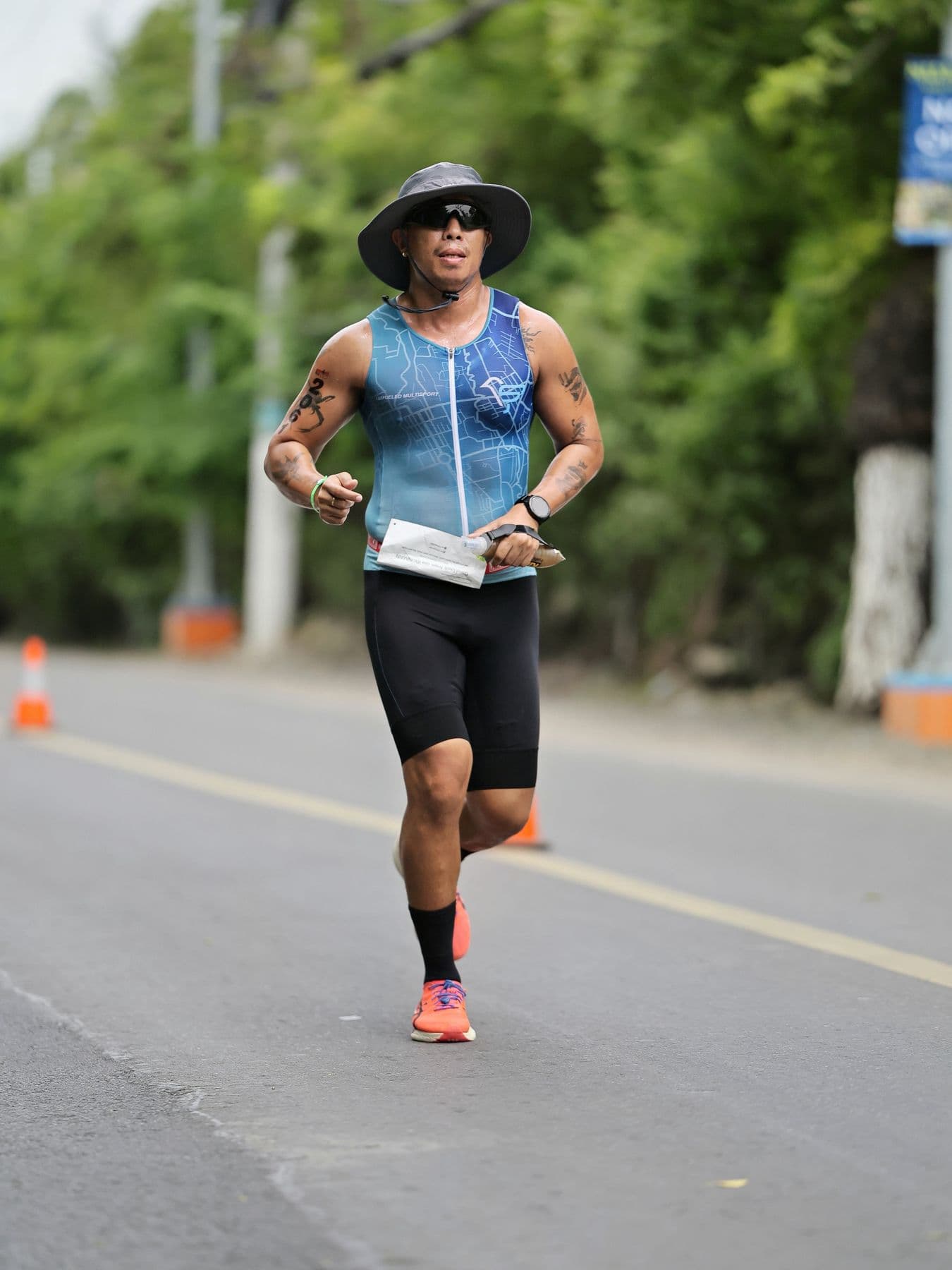 Runner in a sun hat and sleeveless trisuit running along a tree-lined road
