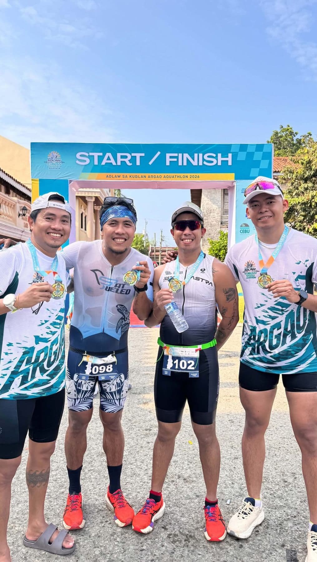 Four triathletes with medals under a Start/Finish arch