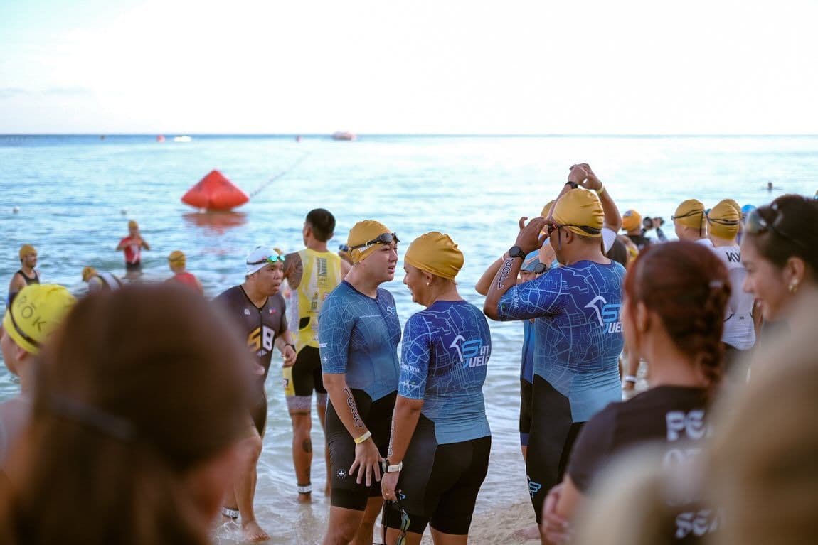 Swimmers in matching caps gathering on the shore before an open-water start