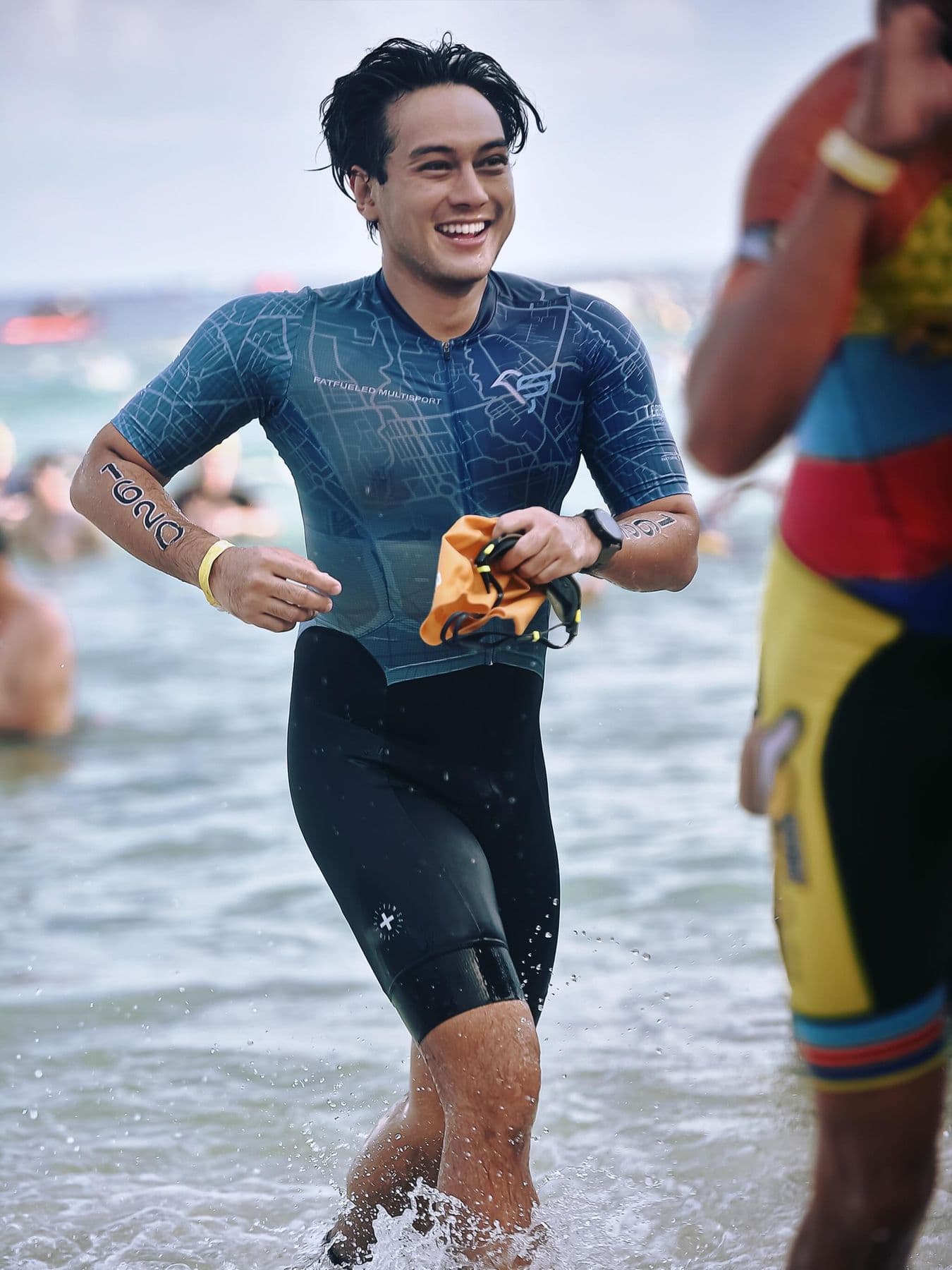 Smiling triathlete in a dark trisuit jogging out of the water