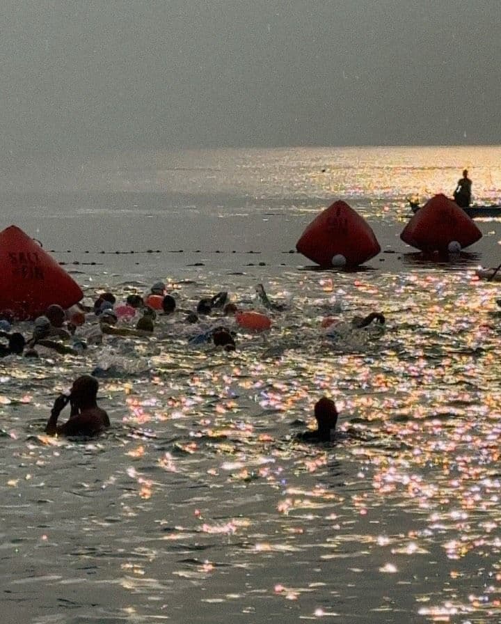 Open-water swimmers at sunrise beside large orange race buoys