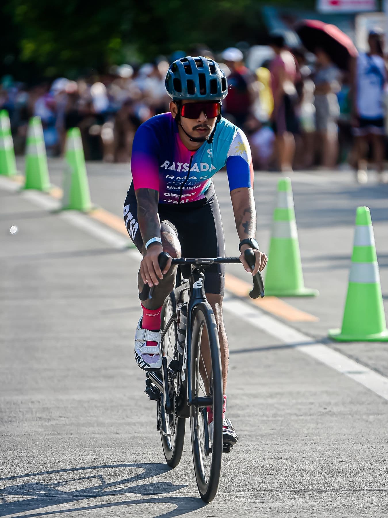 Cyclist in a pink-and-blue kit racing past green traffic cones