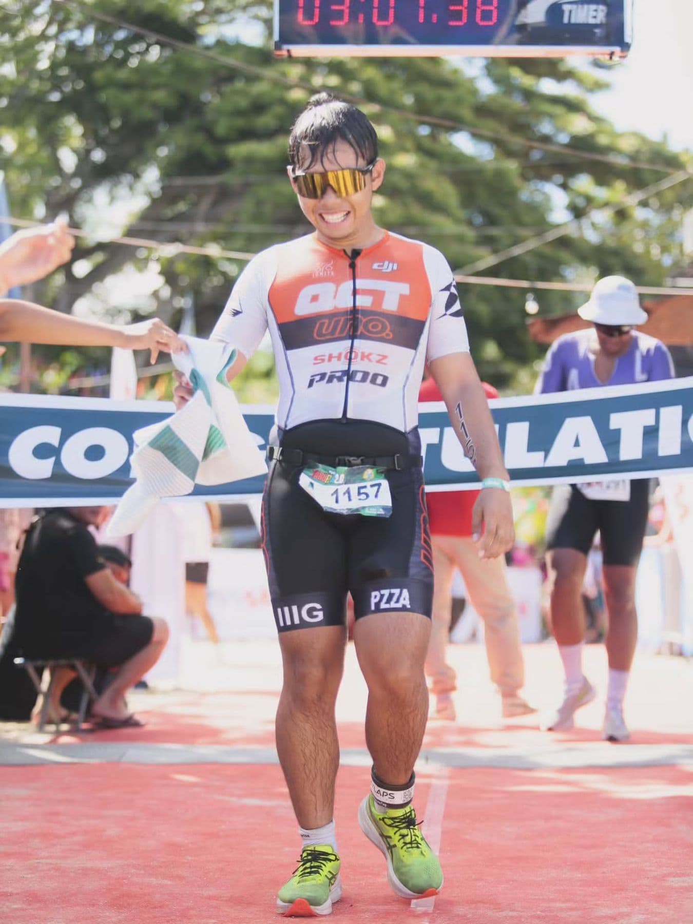 Triathlete in an orange-and-white kit jogging under a Congratulations banner at the finish