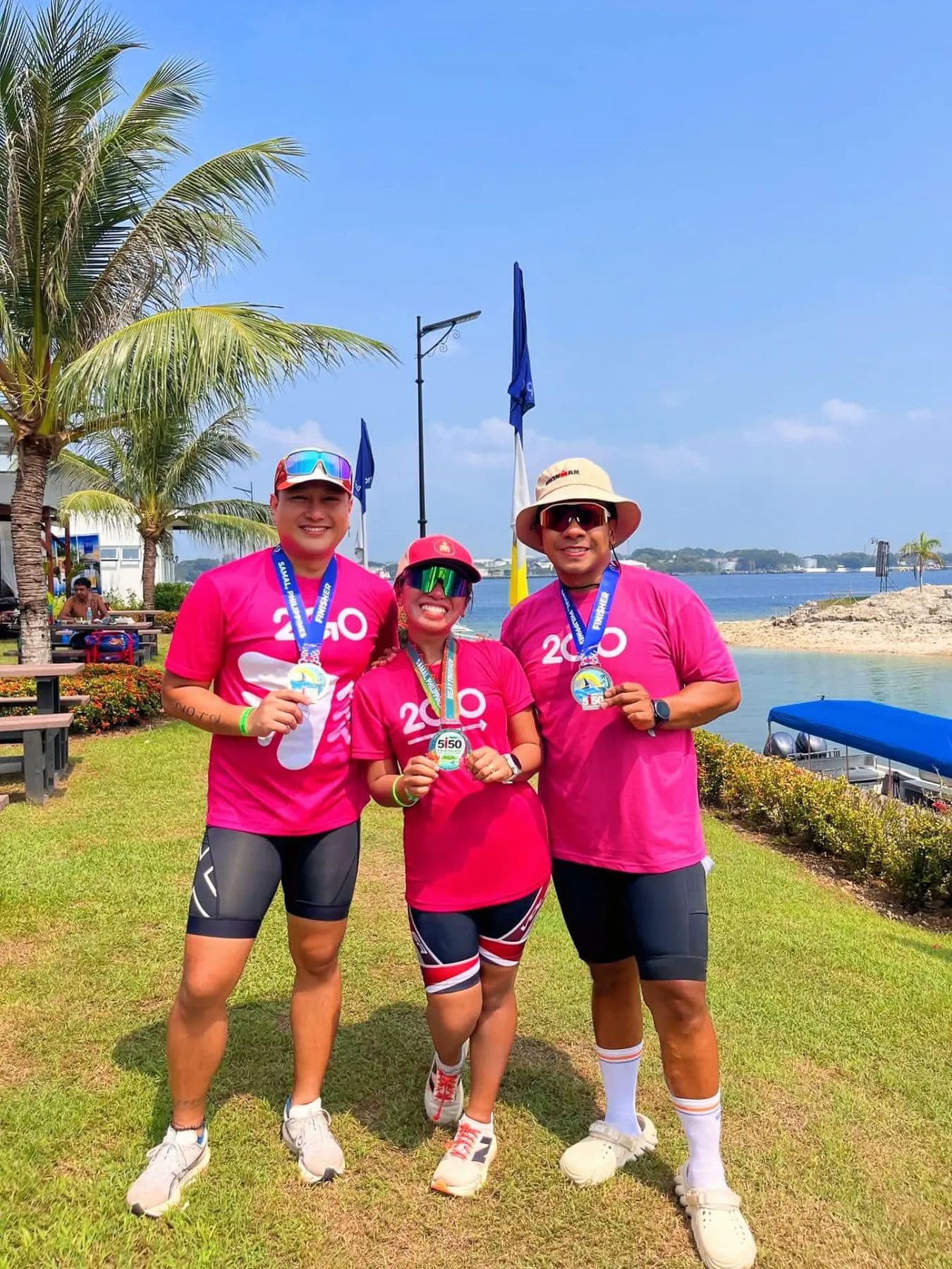 Three athletes in matching pink shirts showing their medals by the sea