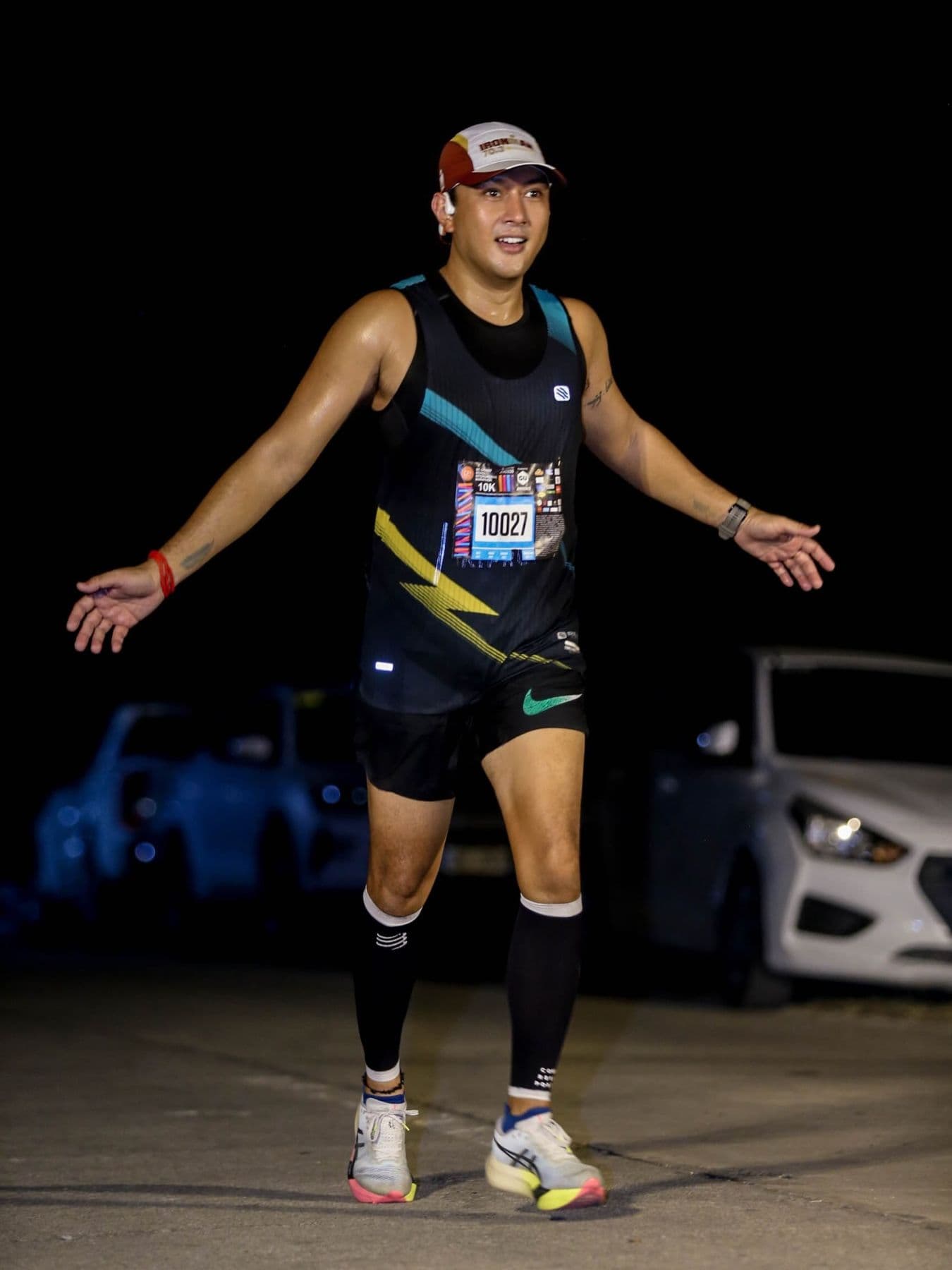 Runner in a black race kit with arms outstretched at a night race
