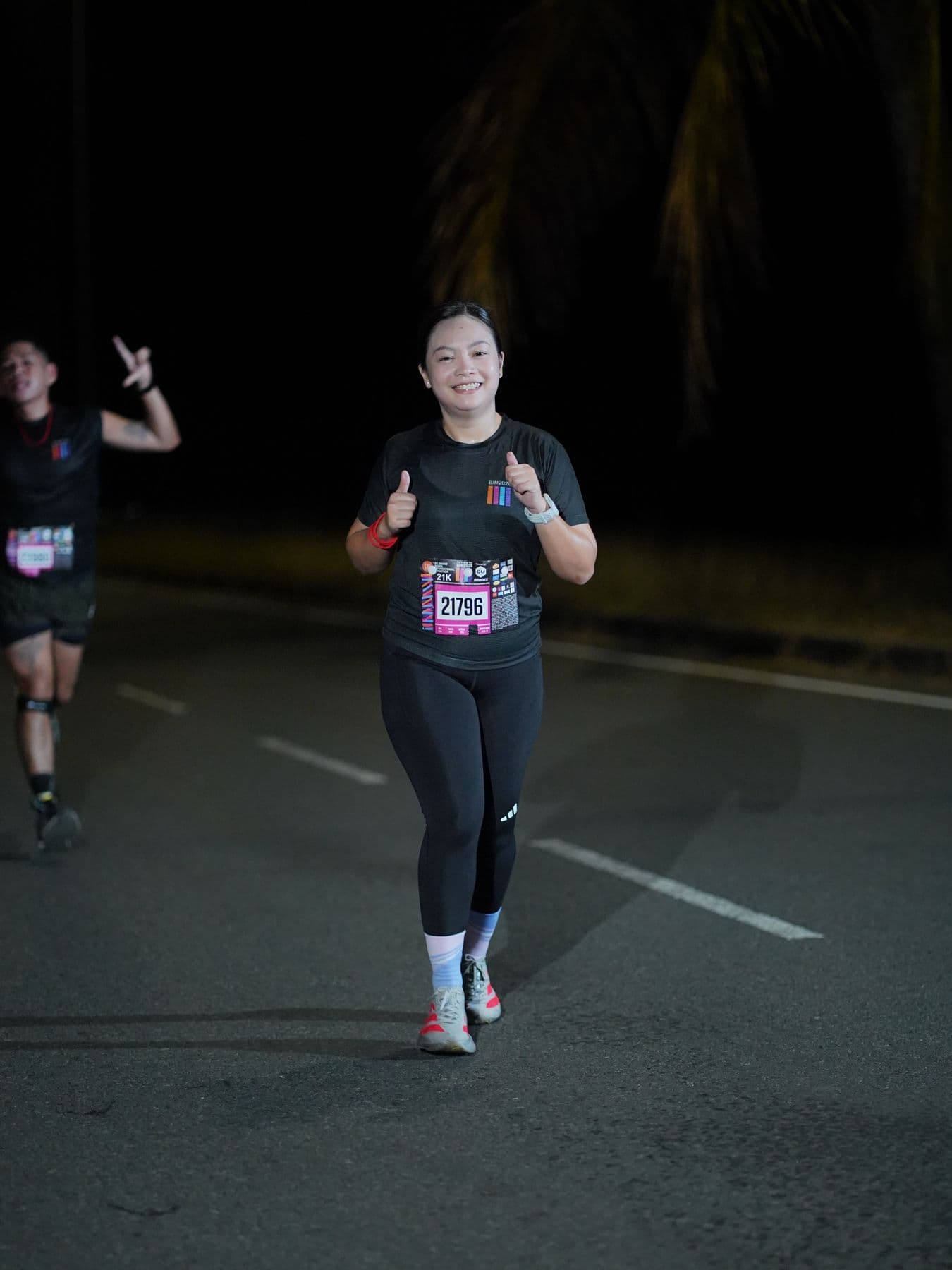 Runner giving a thumbs-up on a dark road during a night race