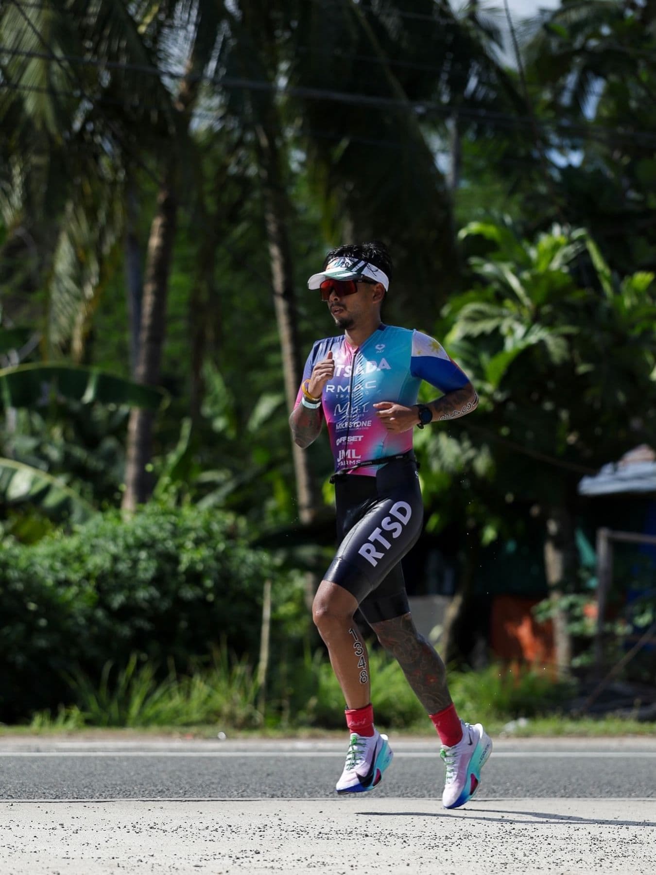 Runner in a triathlon kit striding along a road lined with tropical trees