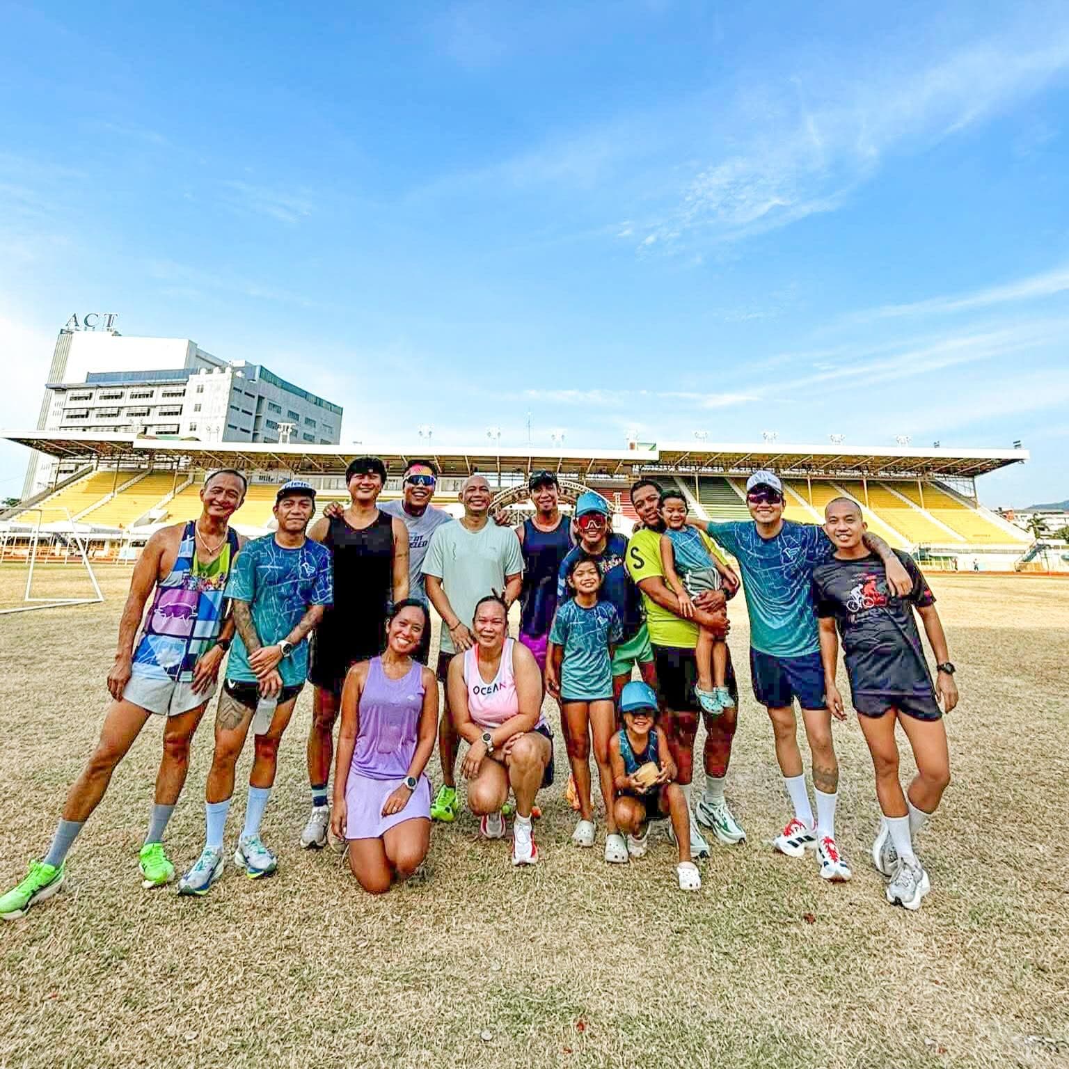Group of runners and families posing on a stadium field