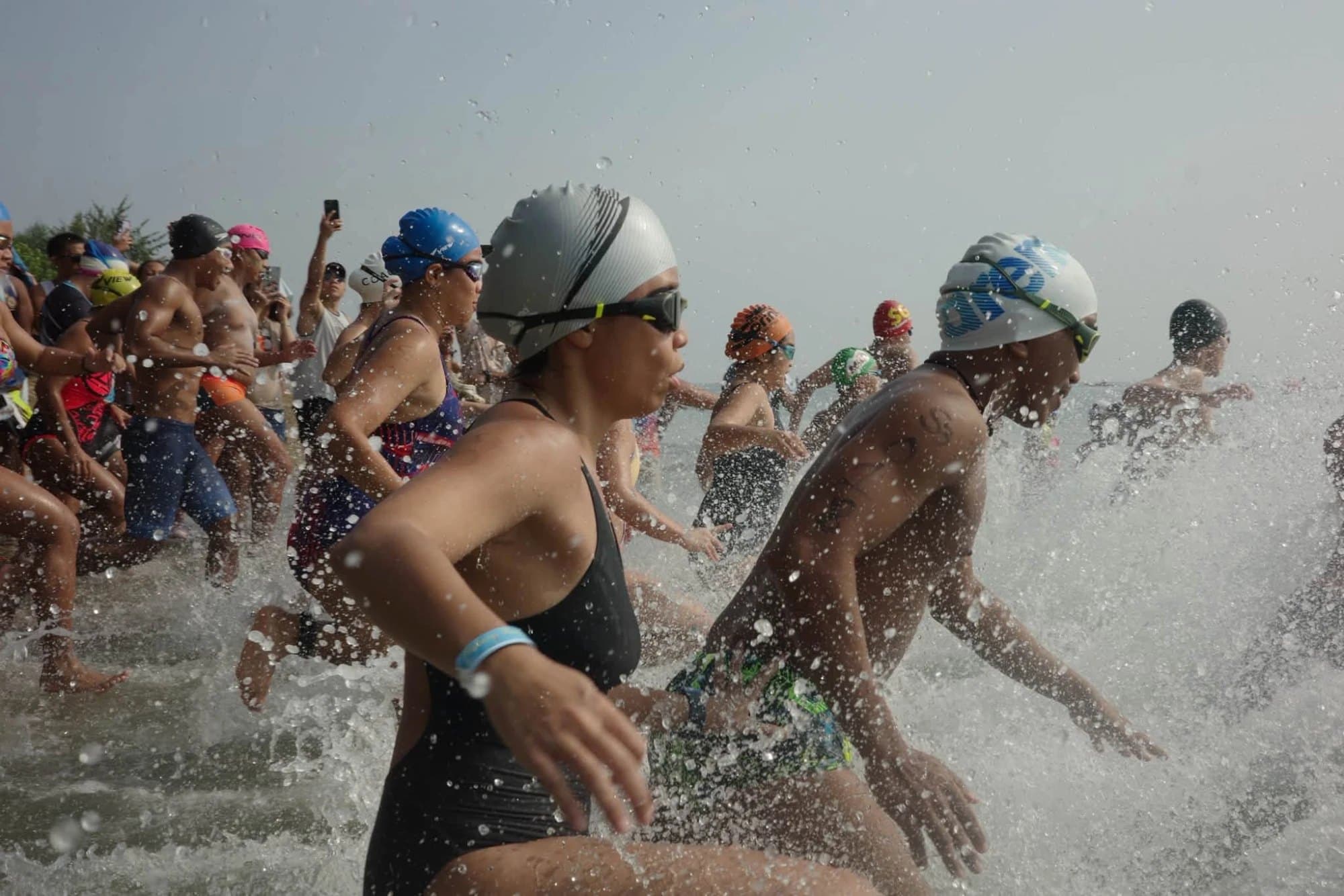 Open-water swimmers in caps and goggles sprinting into the sea at a race start
