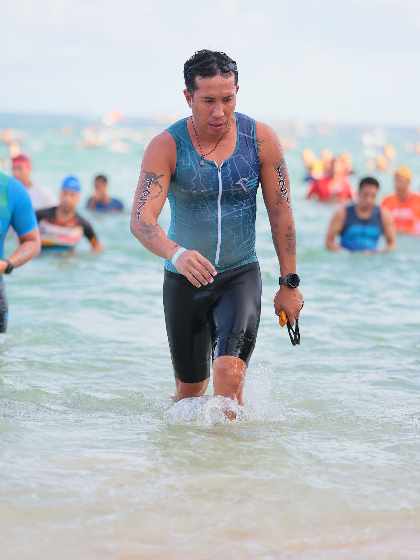 Triathlete in a blue trisuit walking out of the sea after the swim