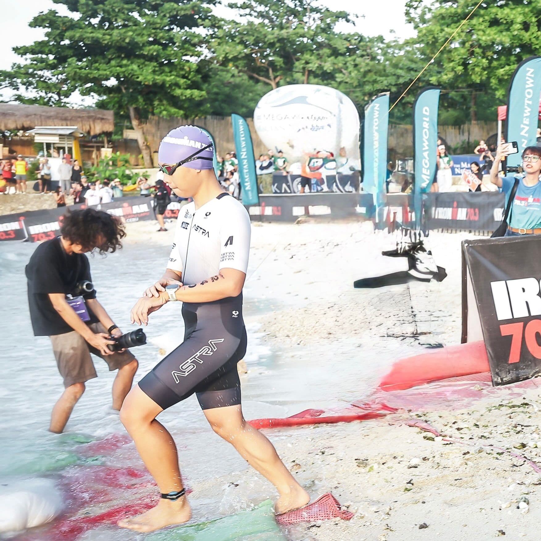 Triathlete running up the beach out of the swim at a race, checking their watch